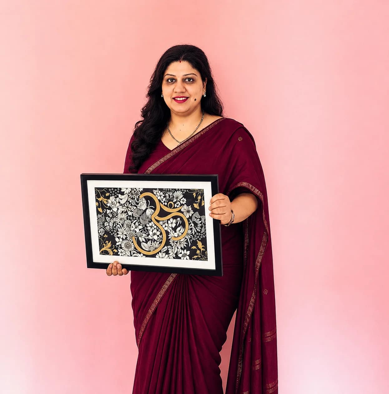 Ayushi Sharma in a maroon saree, holding her framed gold Om painting